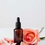 Elegant dropper bottle with pink rose petals on a wooden plate, perfect for aromatherapy or skincare.