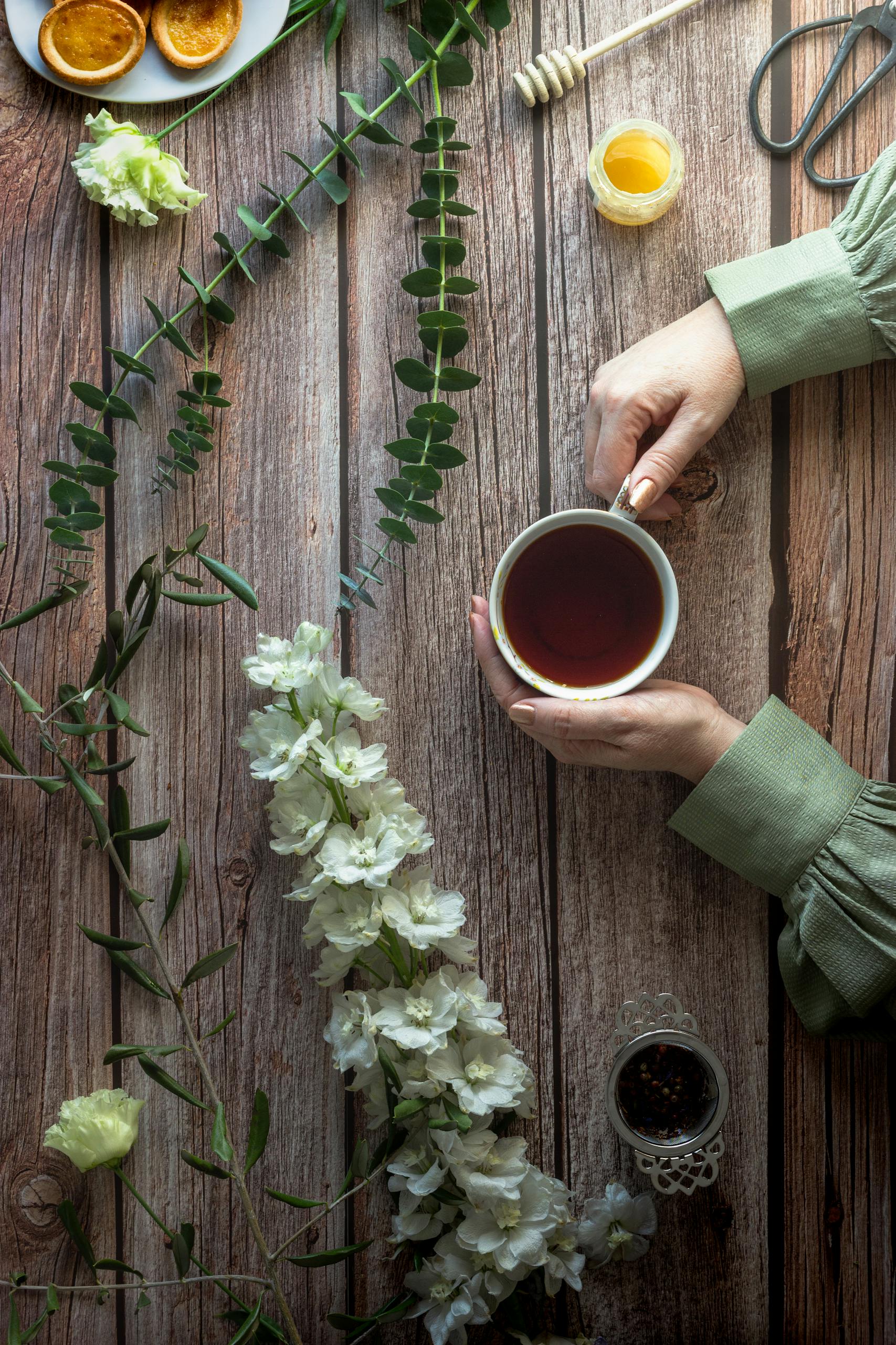 A cozy flat lay of a tea cup held over a wooden table with flowers and honey, evoking a rustic vibe.