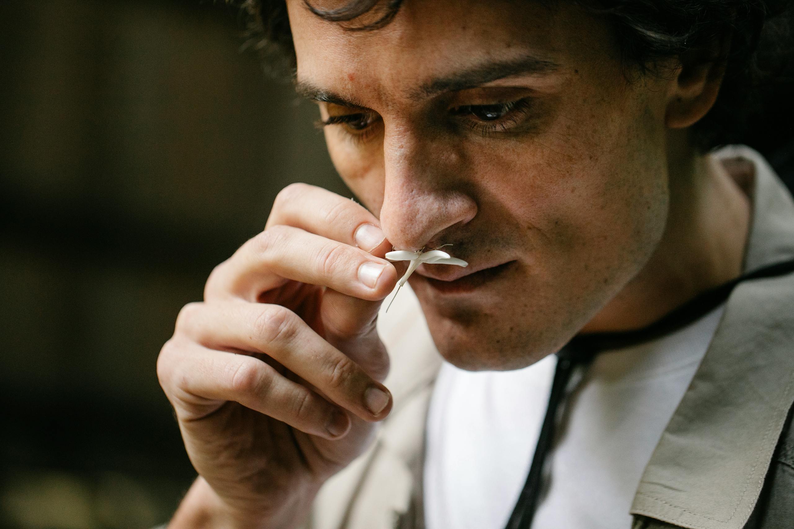 A man thoughtfully smells a delicate white flower in an outdoor setting, enjoying its scent.
