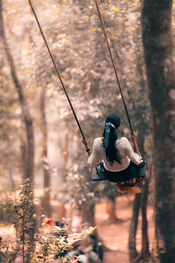 A woman enjoys a peaceful swing ride in a sunlit forest, evoking relaxation and tranquility.