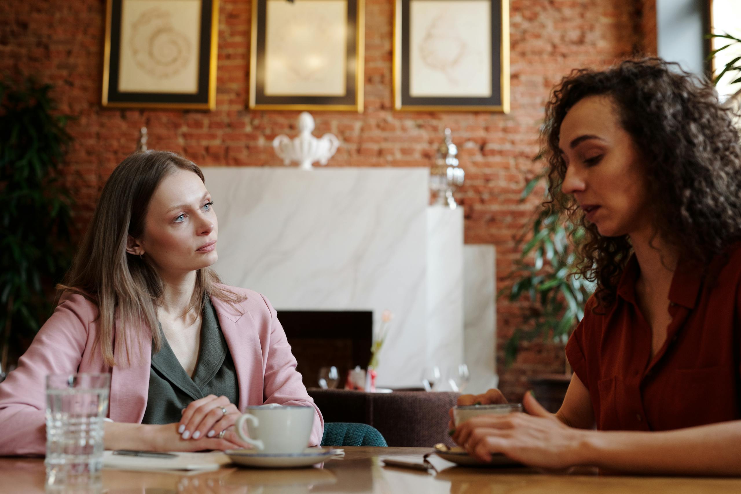 Two women engaged in serious discussion over coffee in a cozy indoor café setting.