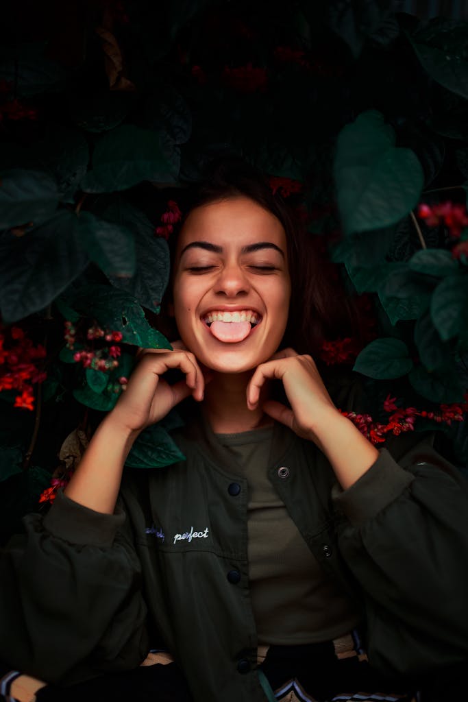 Joyful woman with eyes closed and tongue out surrounded by dark green leaves.