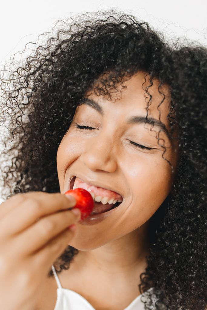 Close-up of a smiling woman enjoying a fresh strawberry, embracing healthy eating.