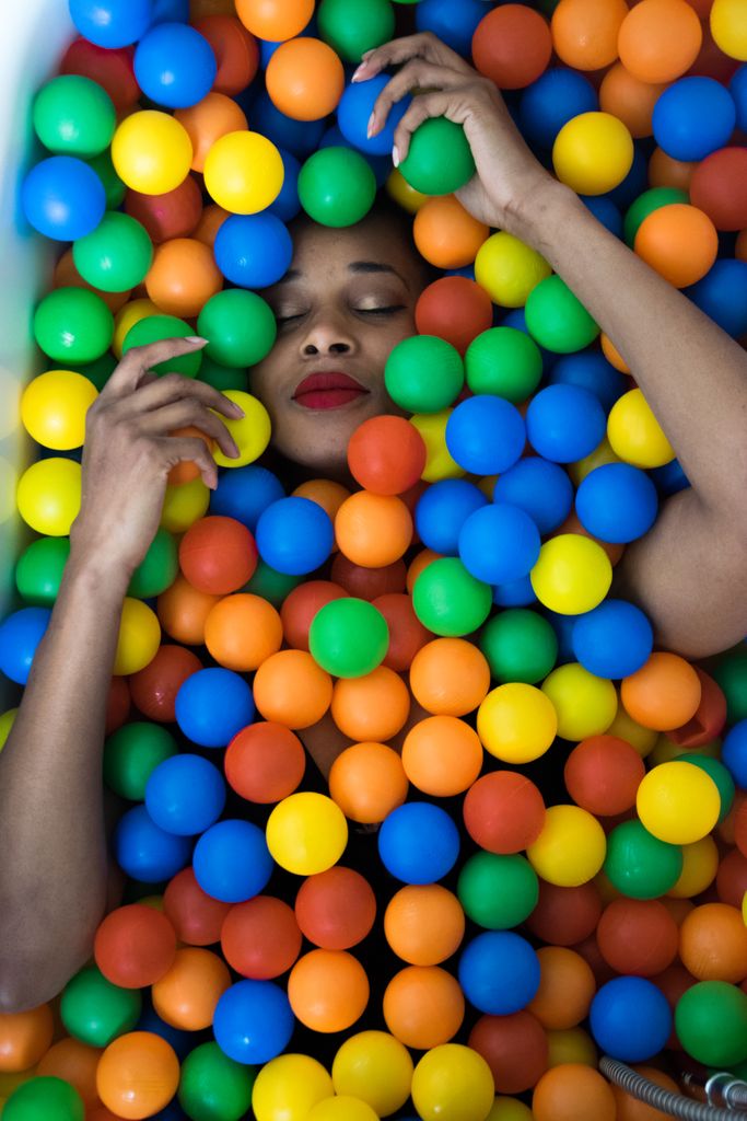 A woman peacefully relaxing, submerged in a colorful ball pit, creating a playful and dreamy atmosphere.