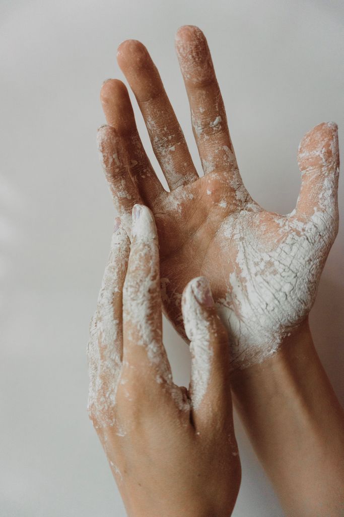 Detailed view of human hands covered in white powder, suggestive of cosmetics or baking flour.